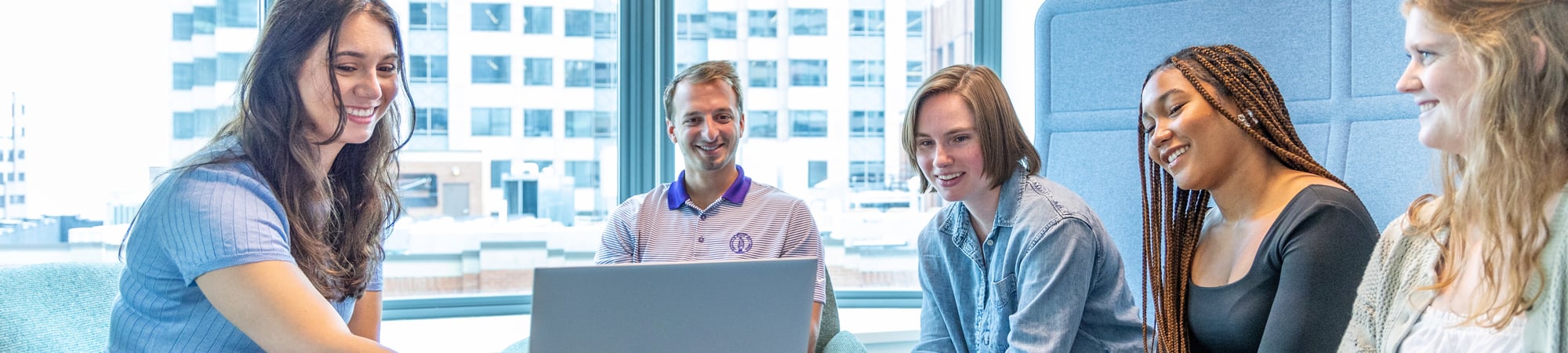 5 people sitting on a couch looking at a laptop.