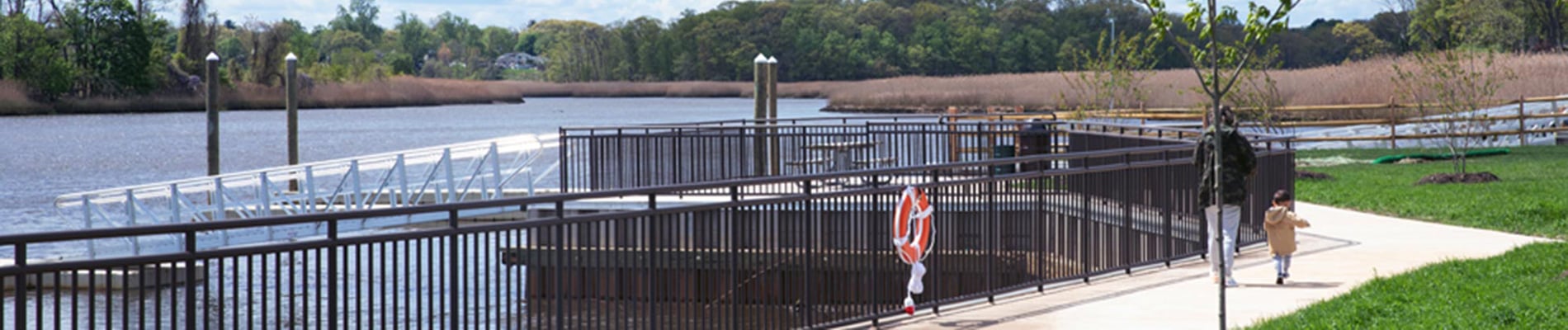 A waterfront walkway with a fence and grass.