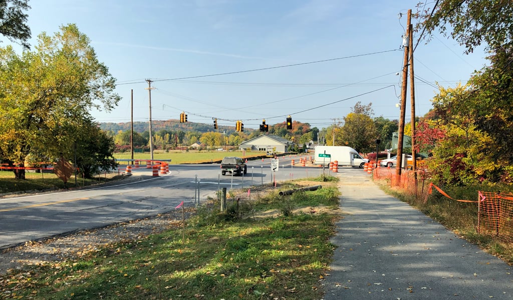 An intersection with traffic light, cars and trees undergoing road construction.