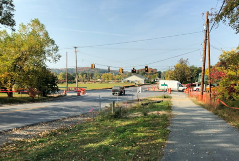 An intersection with traffic light, cars and trees undergoing road construction.