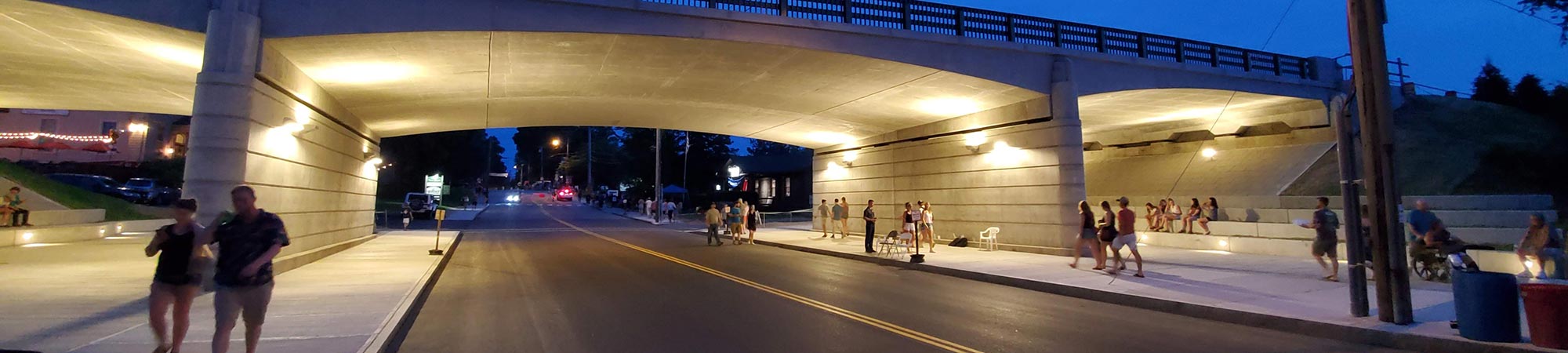 People walk under the newly reconstructed Main Street Bridge at twilight.