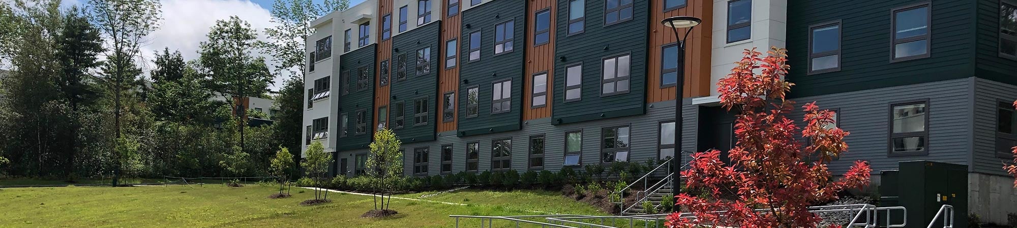 A white, green, and orange student housing building is bordered by accessible paths and green space. 