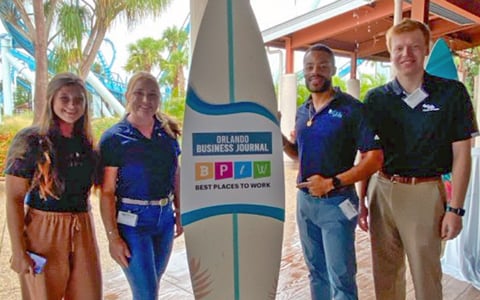 A group of people standing beside a surfboard.