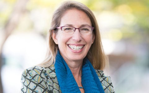 Carol Lurie stands outside wearing glasses and a blue scarf. 