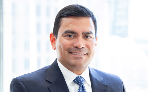 Jorge Luna smiles at the camera wearing a blue blazer and tie.