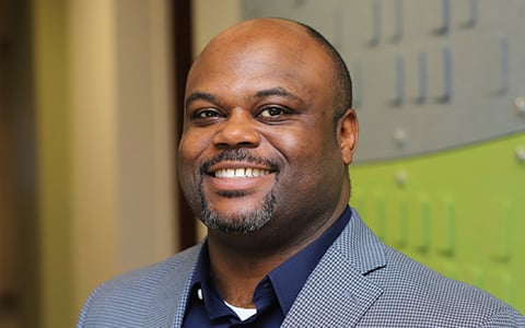 Brandon McAdams smiles at the camera wearing a plaid blazer.