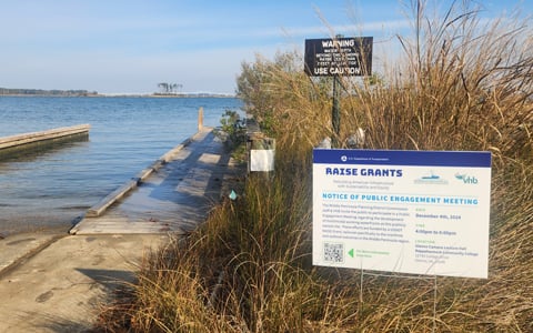 A sign promoting the project at one of the waterfront sites with the water in the background.