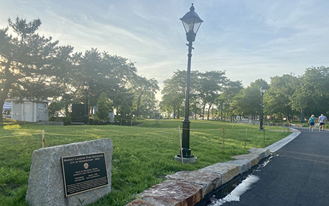 A cement path leading to the waterfront in Newburyport. A plaque on a stone next to the path reads, ”Market Landing Park Expansion, City of Newburyport 2024.” 