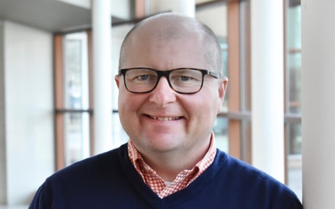 Headshot of Kurt Muller wearing business casual attire smiling in the lobby of an office building.