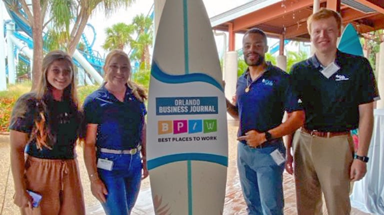 A group of people standing beside a surfboard.