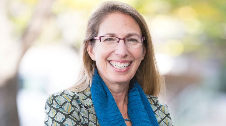 Carol Lurie stands outside wearing glasses and a blue scarf. 