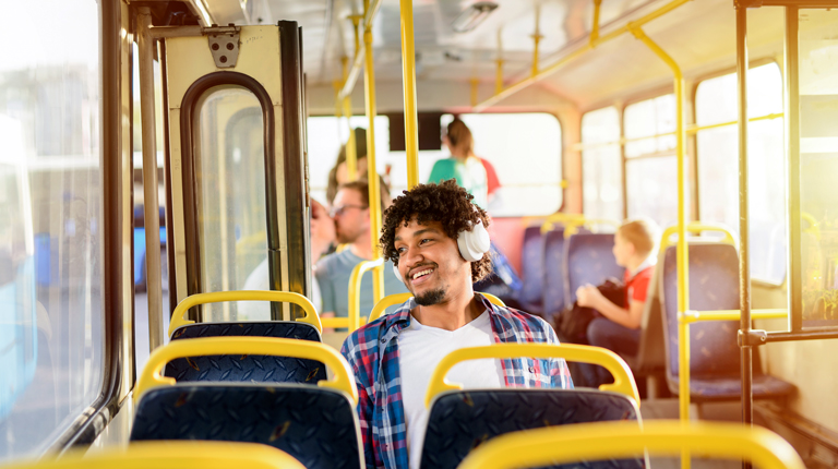 A man is seated on a bus with headphones on looking out the window. 
