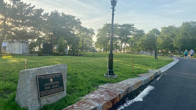 A cement path leading to the waterfront in Newburyport. A plaque on a stone next to the path reads, ”Market Landing Park Expansion, City of Newburyport 2024.” 