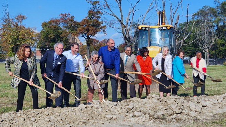 Ten individuals move dirt with shovels to celebrate the project’s groundbreaking.