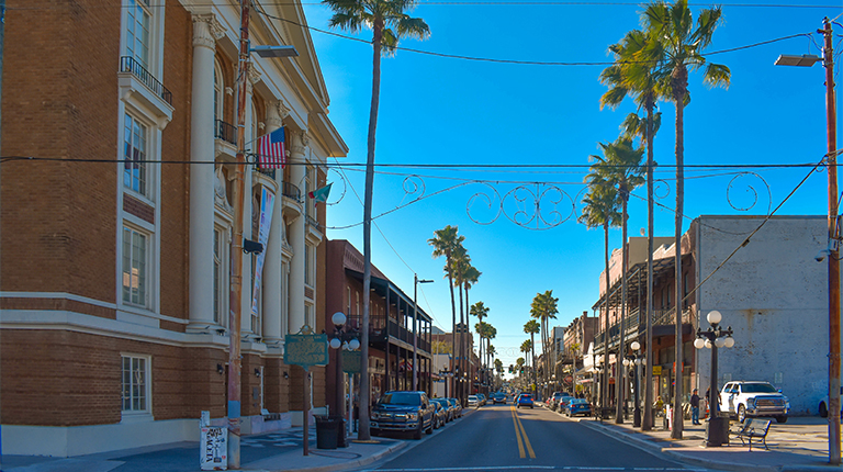 A street lined by historic buildings, cars, and tall palms