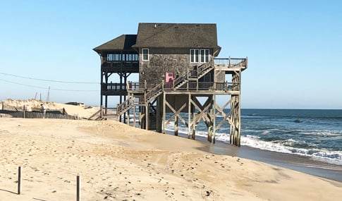 Stilted three story house on the seashore edge during high tide.