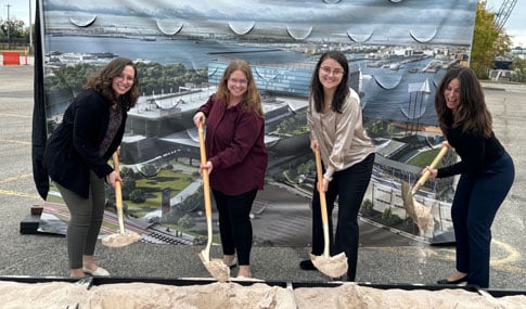 Four members of the design team hold shovels to move dirt.