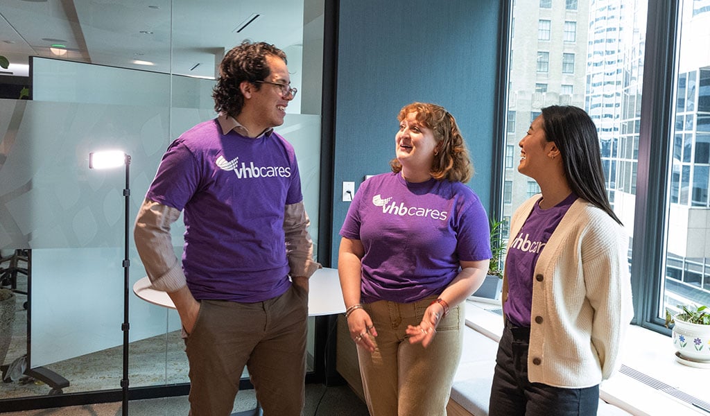 Three VHBers, wearing "VHB Cares" t-shirts talking and smiling in an office setting